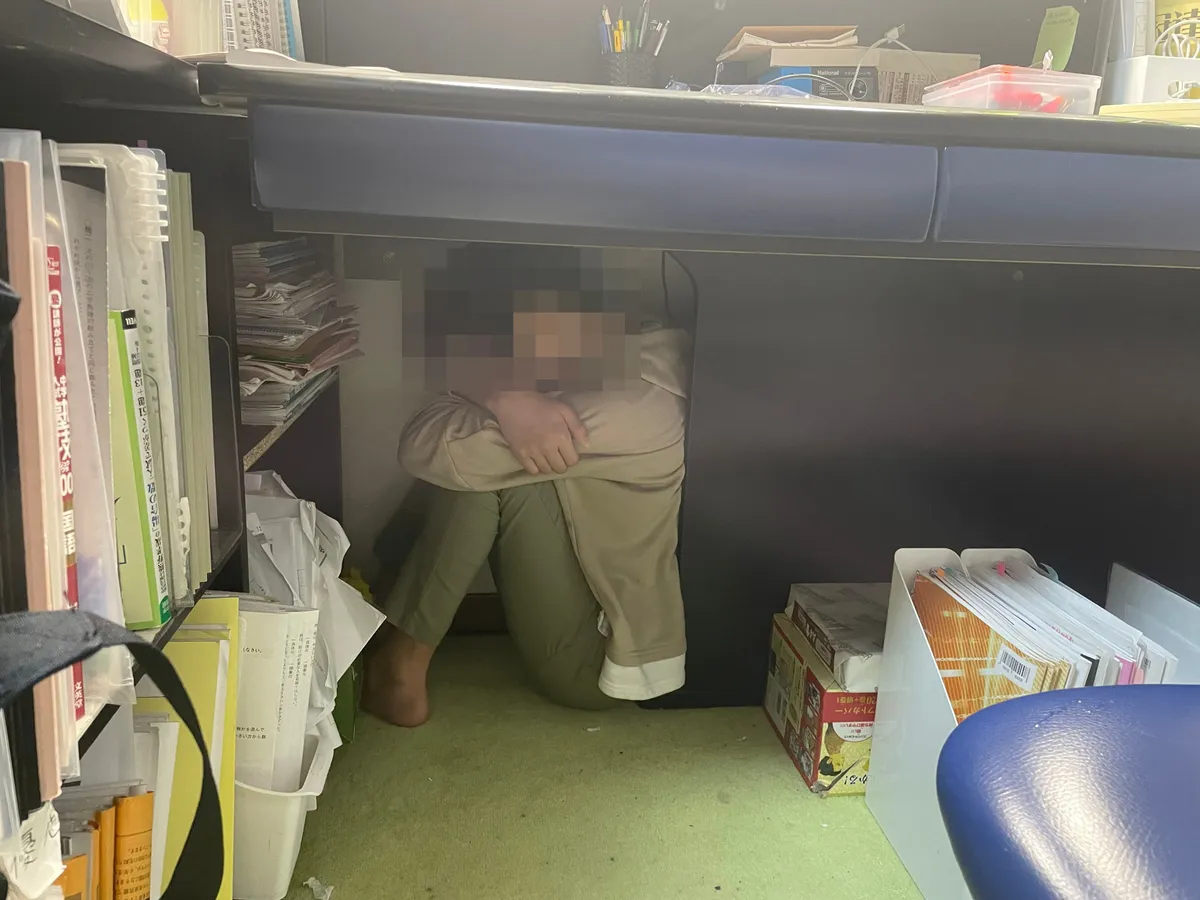机の下でうずくまる息子の様子